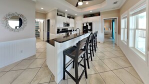 A spacious kitchen with a central island, white cabinetry, and a ceiling fan. - Pelican Point by Miss Kitty’s (Rockport)