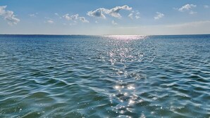 A calm sea with sunlight reflecting off the water, a clear sky, and a distant horizon. - Fisherman Luv by Miss Kitty’s (Rockport)