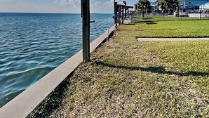 A waterfront property with a grassy area, a concrete walkway, and a building with a blue roof. - Fisherman Luv by Miss Kitty’s (Rockport)