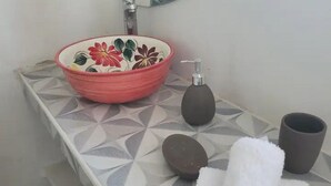 Ein Badezimmer mit einem geometrisch gemusterten Waschtisch, einem roten floralen Waschbecken, einem Seifenspender, einem Handtuch und einer Tasse.