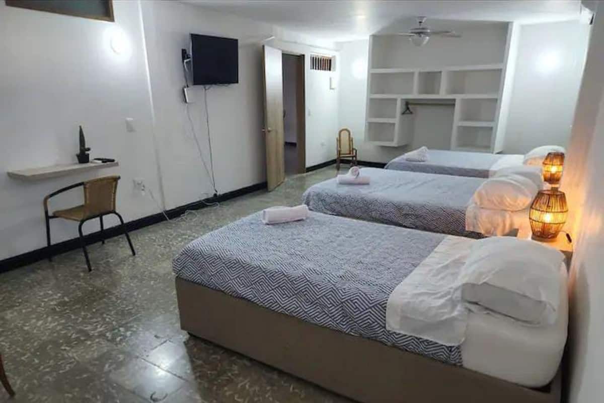 A hotel room with two beds, a desk, a chair, a TV, and a shelf with storage.