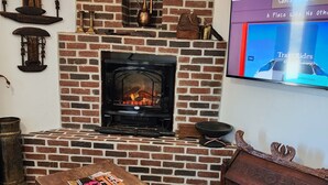 A cozy living room with a brick fireplace, a wooden coffee table with magazines, a woven rug, and a television displaying a travel show. - Come experience a taste of Africa nestled in the foothills of Santa Fe.  (Santa Fe)