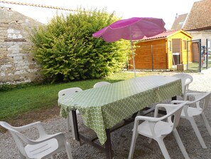 A table set outdoors with a green tablecloth, surrounded by white plastic chairs.