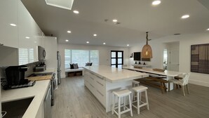 A modern kitchen with a central island, white cabinetry, and a large window with blinds. - Modern Beach LakeFront House in Miami ! (Miami)