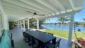 A covered outdoor dining area with a view of a lake, a table with chairs, and a kayak with paddles. - Modern Beach LakeFront House in Miami ! (Miami)