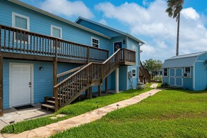 A two-story building with a wooden staircase leading to a balcony, a front door, and a small adjacent structure.