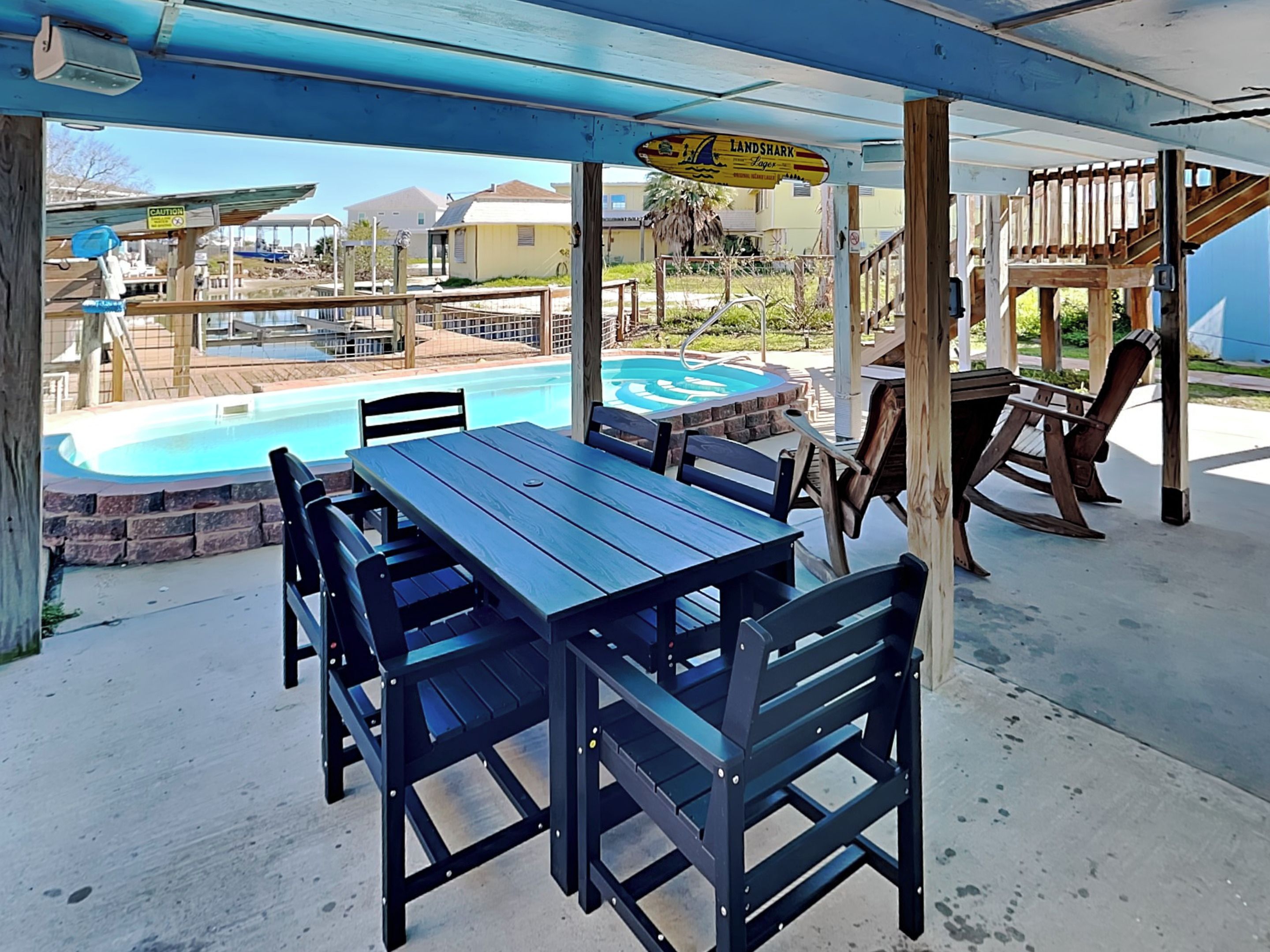 A covered patio area with a pool, wooden tables and chairs, and a sign reading "Land Shark".
