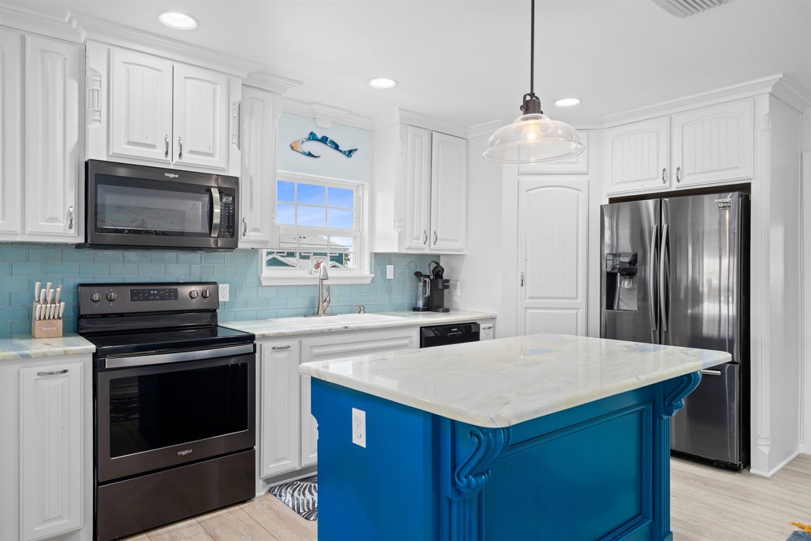 A modern kitchen with white cabinetry, a blue accent wall, stainless steel appliances, and a large island.