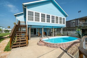 A two-story house with a swimming pool, a wooden staircase, and a covered patio area.