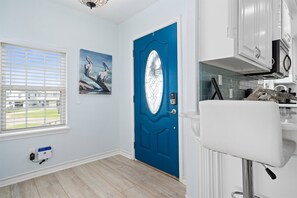 A room with a blue door, a window with blinds, a white sink, and a painting of pelicans.