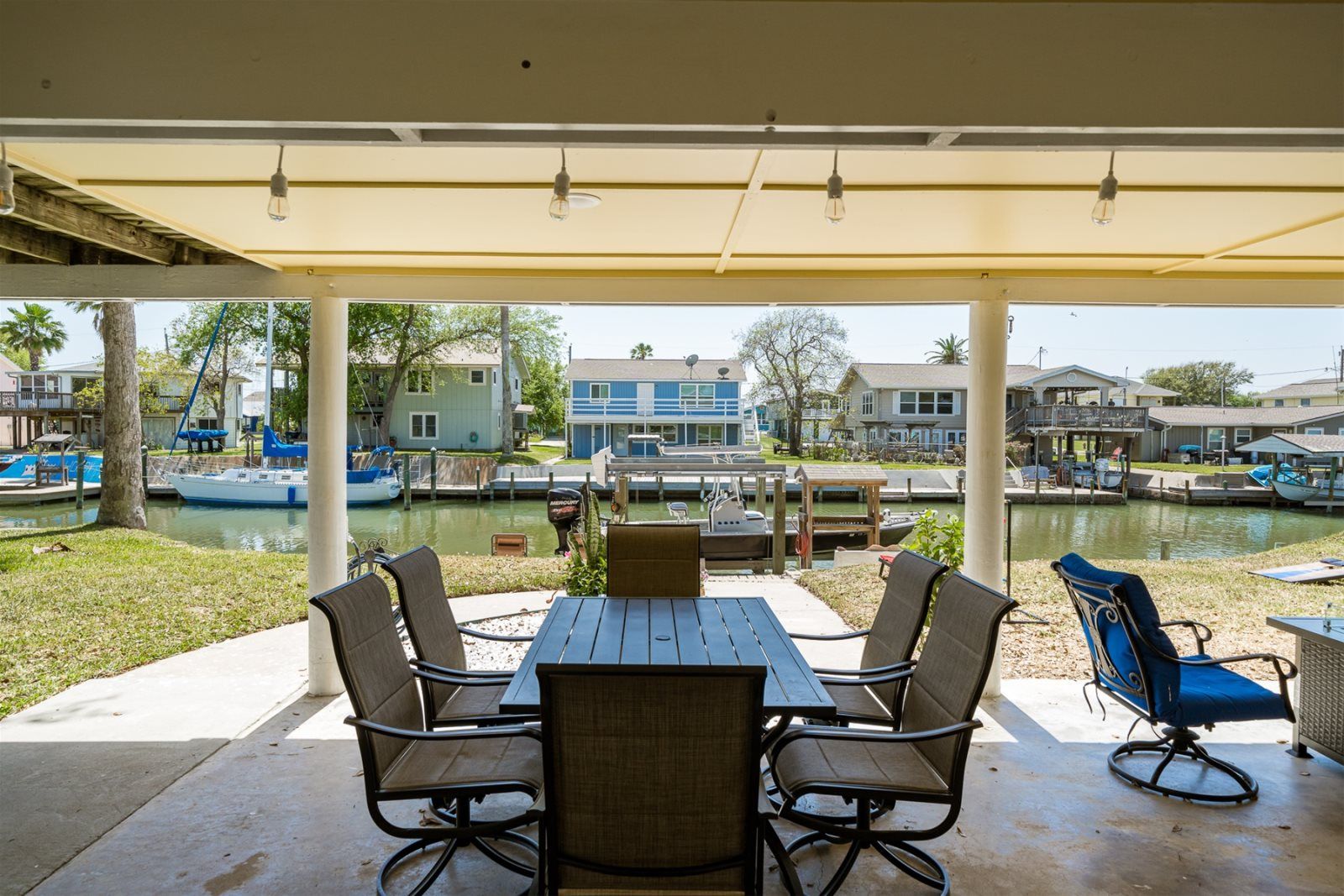 Un espace extérieur abrité, aménagé pour les repas, avec vue sur un port de plaisance et des bateaux.