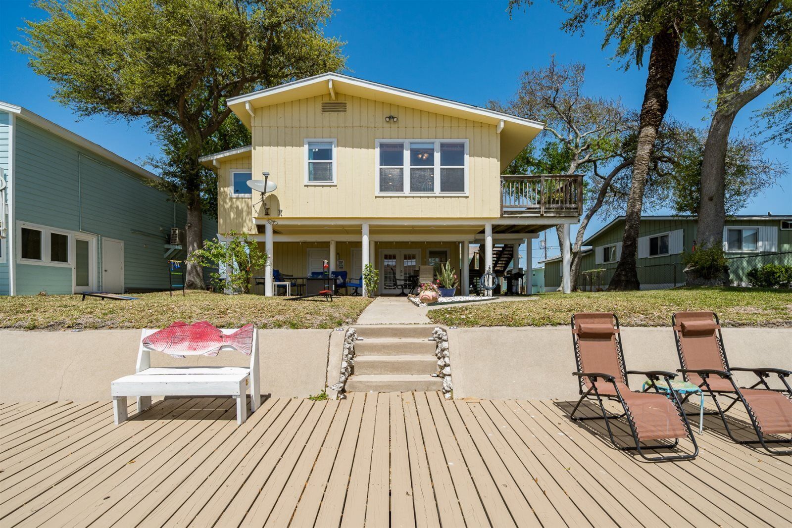 A two-story building with a balcony, a covered porch, and a wooden deck with lounge chairs.