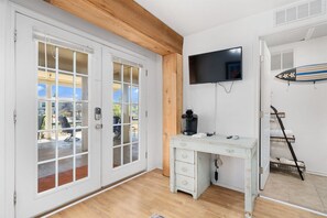 A room with a wooden ceiling, a white desk with drawers, a mounted TV, and a surfboard on the wall. - Catch & Play on Estes Bay by Miss Kitty’s (Rockport)
