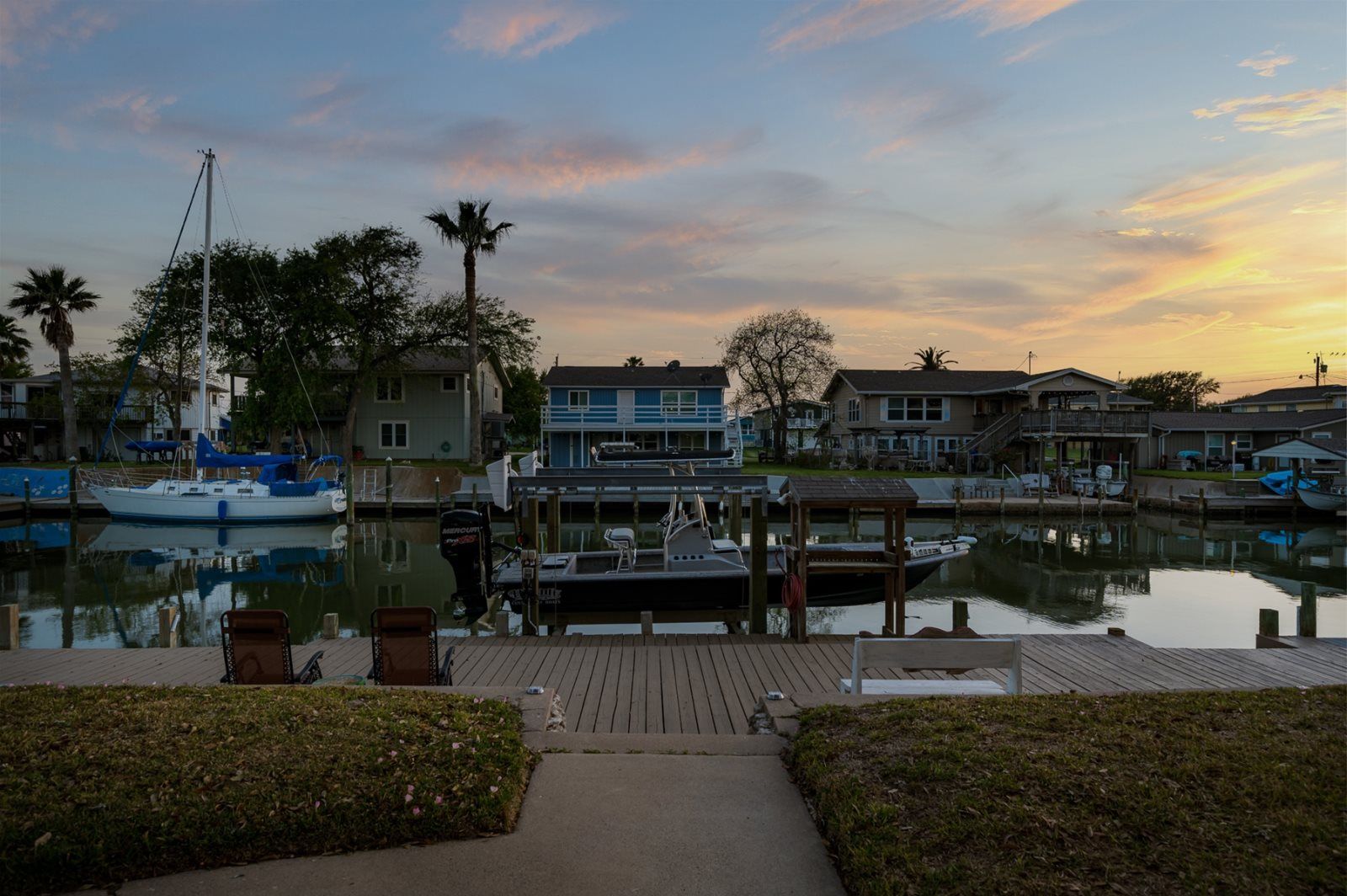 A marina with docked boats, a wooden walkway, and residential buildings in the background.