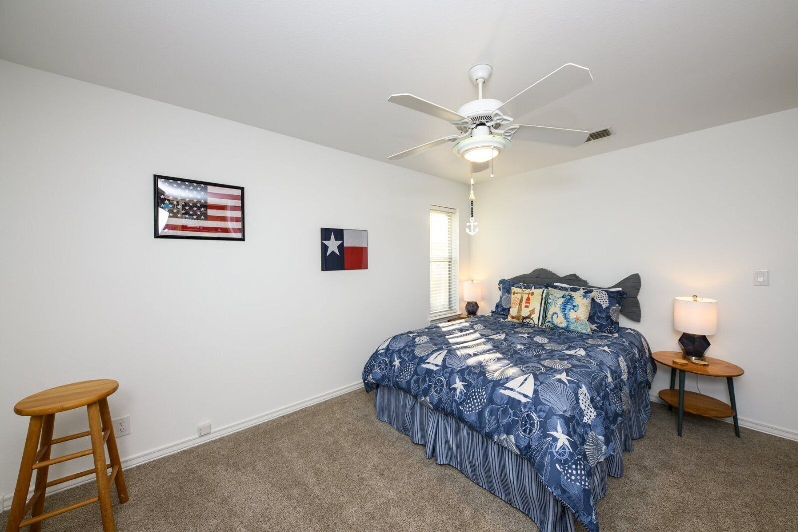 A bedroom with a bed, a ceiling fan, a nightstand with a lamp, and two flags on the wall.