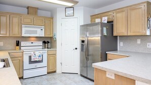 A modern kitchen with wooden cabinets, stainless steel appliances, and a white door. - Attitude Adjustment by Miss Kitty’s (Rockport)