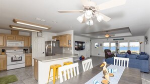 A modern kitchen with a central island, a dining area with a view, and a living room with a sofa and a view. - Attitude Adjustment by Miss Kitty’s (Rockport)
