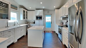 Uma cozinha moderna com armários brancos, eletrodomésticos de aço inoxidável e piso de madeira em padrão herringbone.