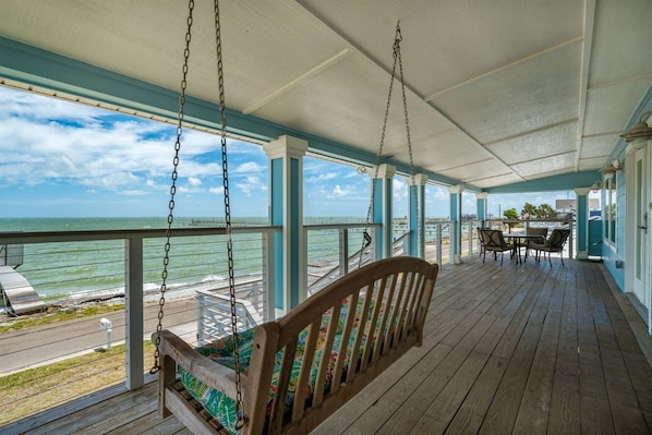A covered porch with a swing, a table with chairs, and a view of the ocean.