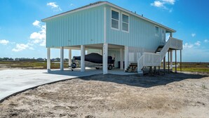 A light blue beach house with a covered porch, a staircase, and a covered vehicle. - Birds on the Bay by Miss Kitty’s (Rockport)