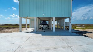 A light blue building with a covered area and a boat docked underneath. - Birds on the Bay by Miss Kitty’s (Rockport)
