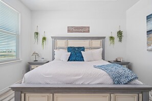 Ein ordentlich eingerichtetes Schlafzimmer mit einem Bett, Nachttischen und hängenden Pflanzen.