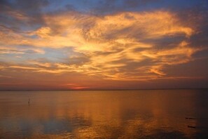 A sunset over a calm sea with a person standing on the shore. - Frisco Flats by Miss Kitty’s (Rockport)