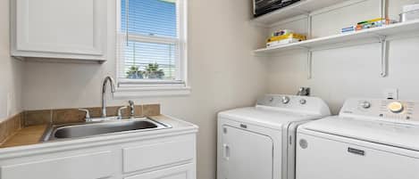 A laundry area with a washing machine, dryer, and a window with blinds.