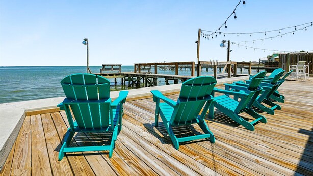 A wooden deck with green chairs and a view of the ocean.
