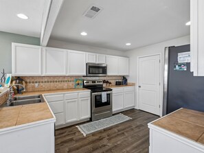 A kitchen with white cabinets, a stainless steel oven, a microwave, and a refrigerator. - Frisco Flats by Miss Kitty’s (Rockport)