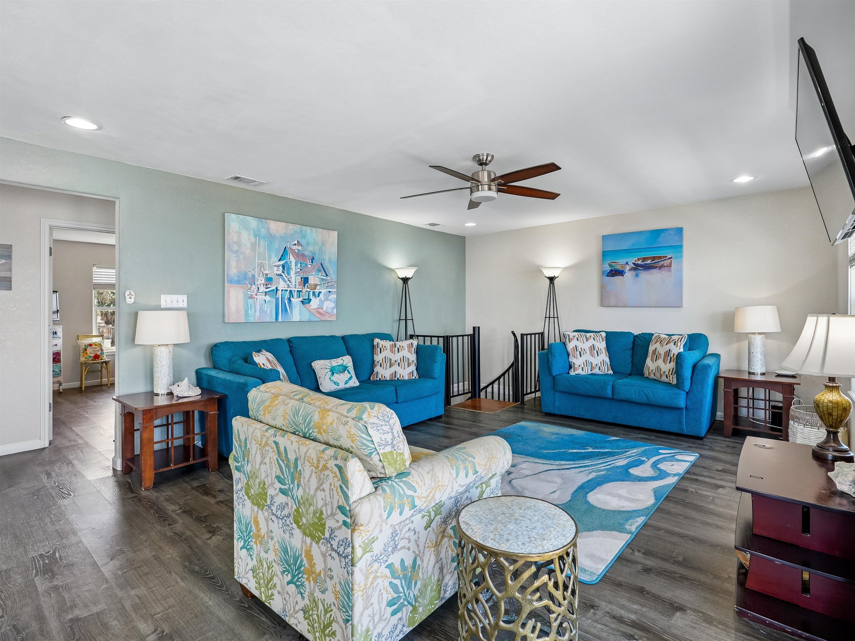 A living room with two blue sofas, a patterned armchair, a round side table, and a ceiling fan.