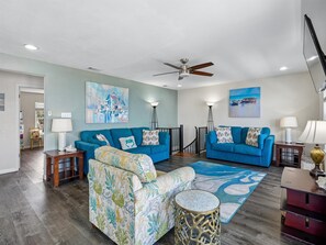 A living room with two blue sofas, a patterned armchair, a round side table, and a ceiling fan. - Frisco Flats by Miss Kitty’s (Rockport)