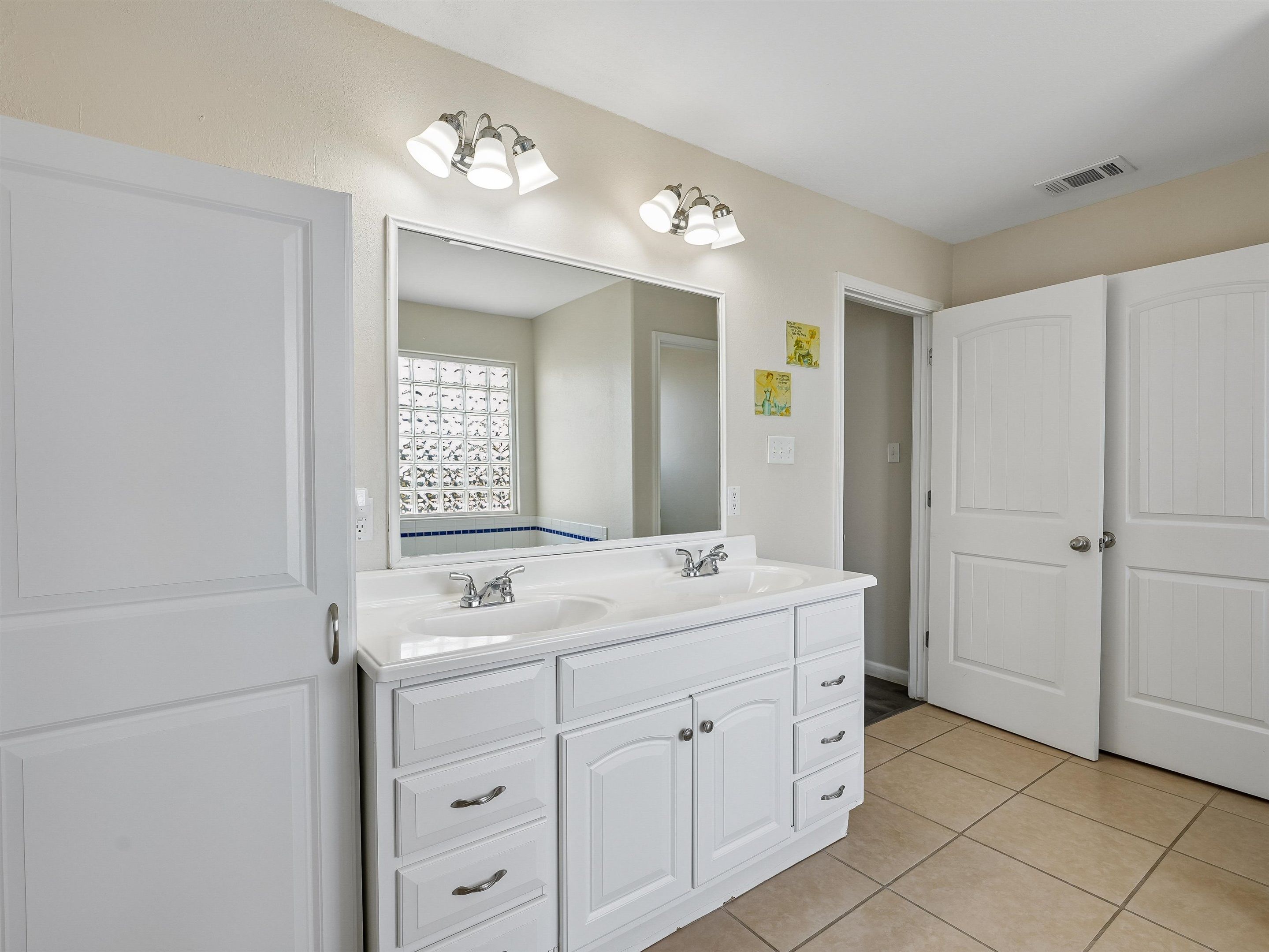 A bathroom with a double sink vanity, a large mirror, and a light fixture above the mirror.
