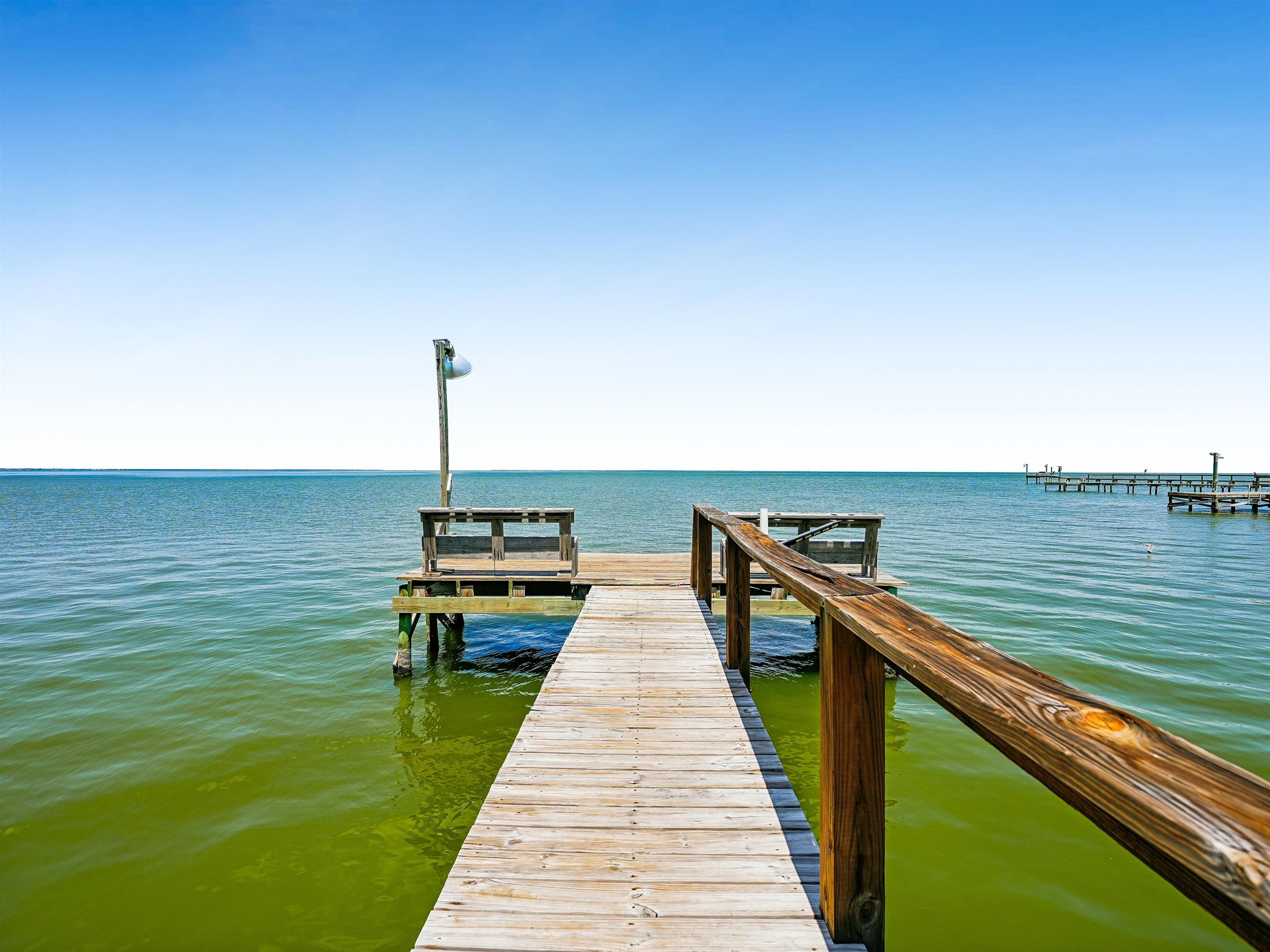 A wooden pier extending into calm waters with a bench and a lamp post.