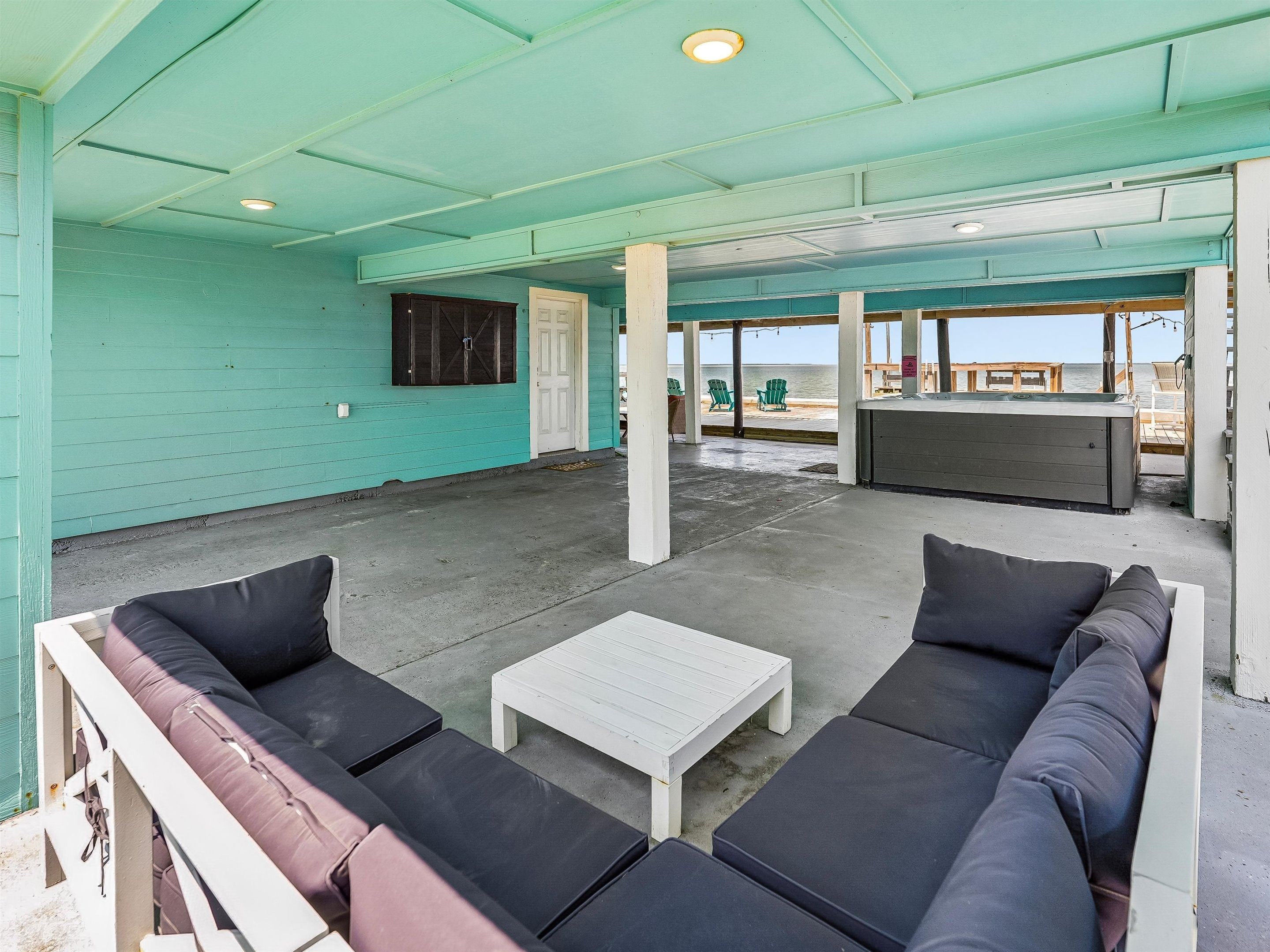 A covered outdoor seating area with a pool table, lounge chairs, and a view of the beach.