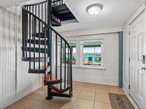 A spiral staircase with wooden steps and black railings, leading to a landing with a view of outdoor seating by a body of water. - Frisco Flats by Miss Kitty’s (Rockport)