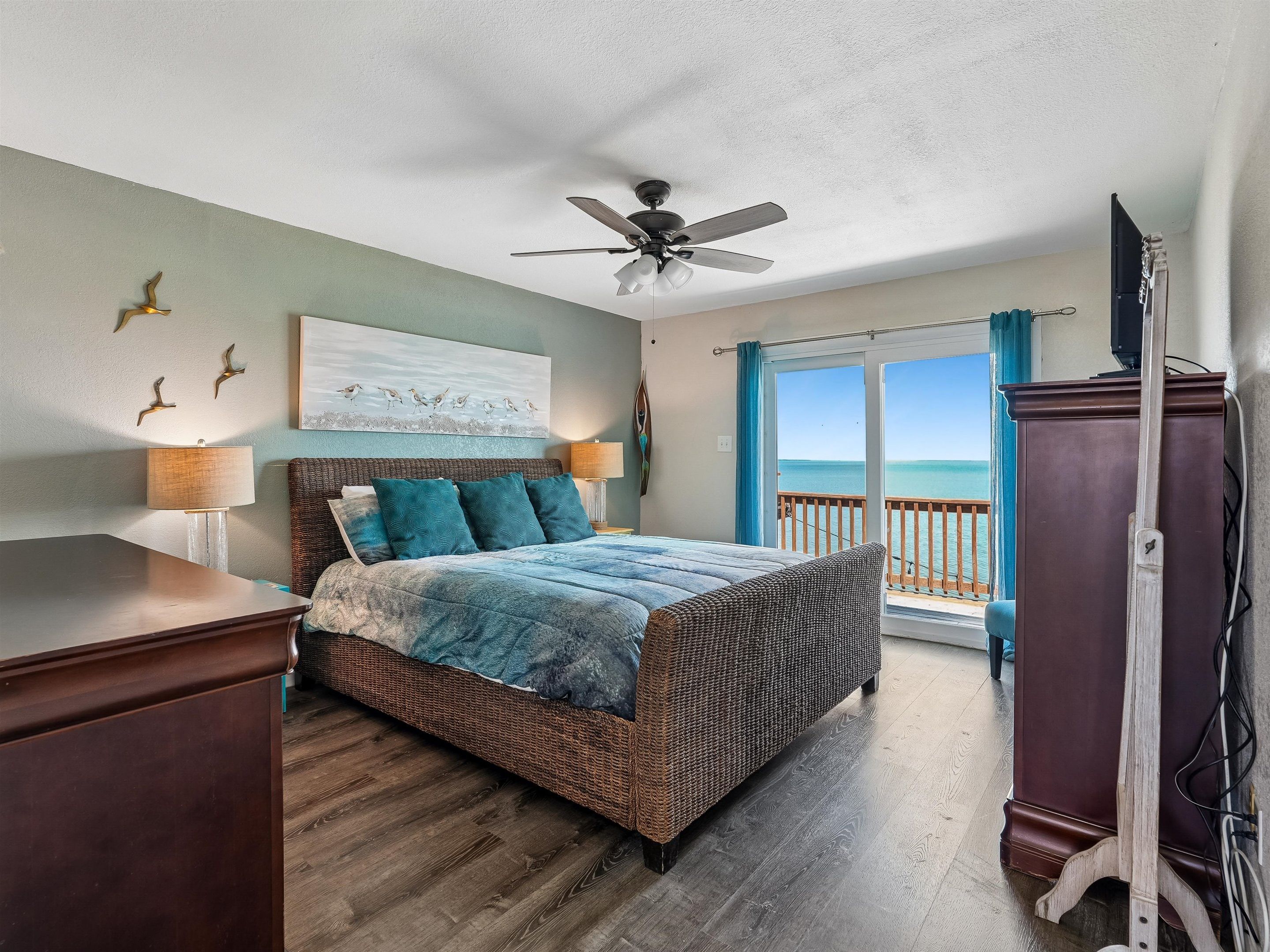 Un dormitorio con cama, ventilador de techo, vista al océano y cómoda de madera.