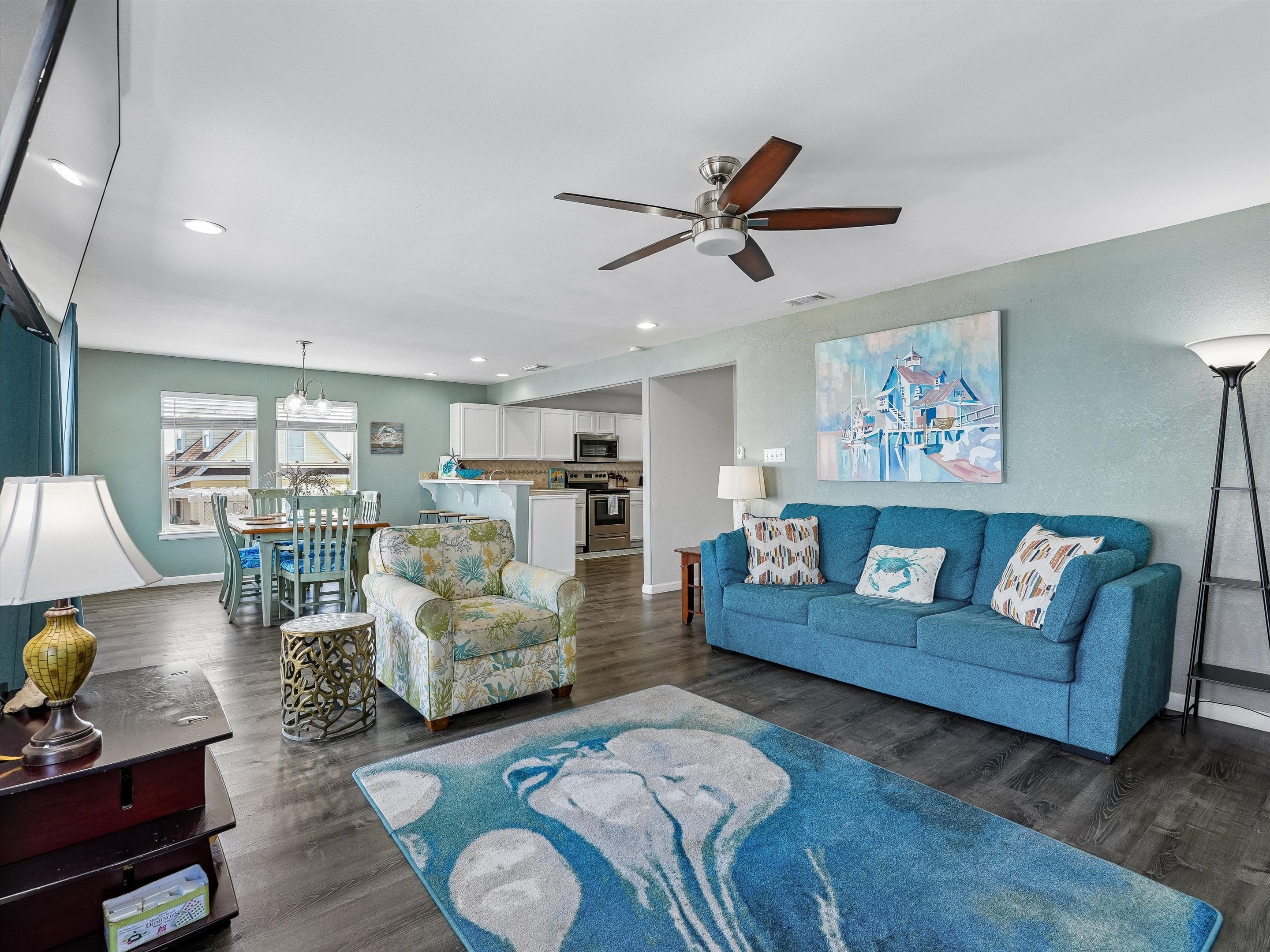 A modern living room with a blue sofa, a ceiling fan, and a kitchen in the background.