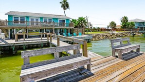 A waterfront property with a wooden dock, a two-story building with balconies, and a clear view of the water.