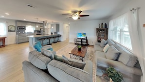 A modern living room with a grey sofa, a coffee table, and a TV. There's a kitchen in the background with grey cabinets and a microwave. - Trout Tank by Miss Kitty’s (Rockport)