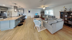 A modern kitchen with a bar area, a grey sofa, and a bookshelf with decorative items. - Trout Tank by Miss Kitty’s (Rockport)
