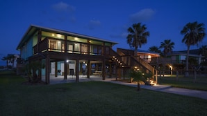 A two-story house with a covered patio area, outdoor seating, and a staircase leading to an upper deck. - Trout Tank by Miss Kitty’s (Rockport)