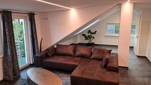 A modern living room with a brown sectional sofa, a small round table, and a potted plant. - Luxurious apartment (new build) with feel-good guarantee.... Temporary living (Ispringen)