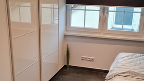 A bedroom with a bed, a window, a radiator, and a wardrobe. - Luxurious apartment (new build) with feel-good guarantee.... Temporary living (Ispringen)