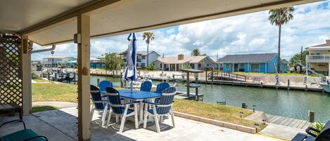 A covered patio with a table and chairs, overlooking a marina with boats and houses.