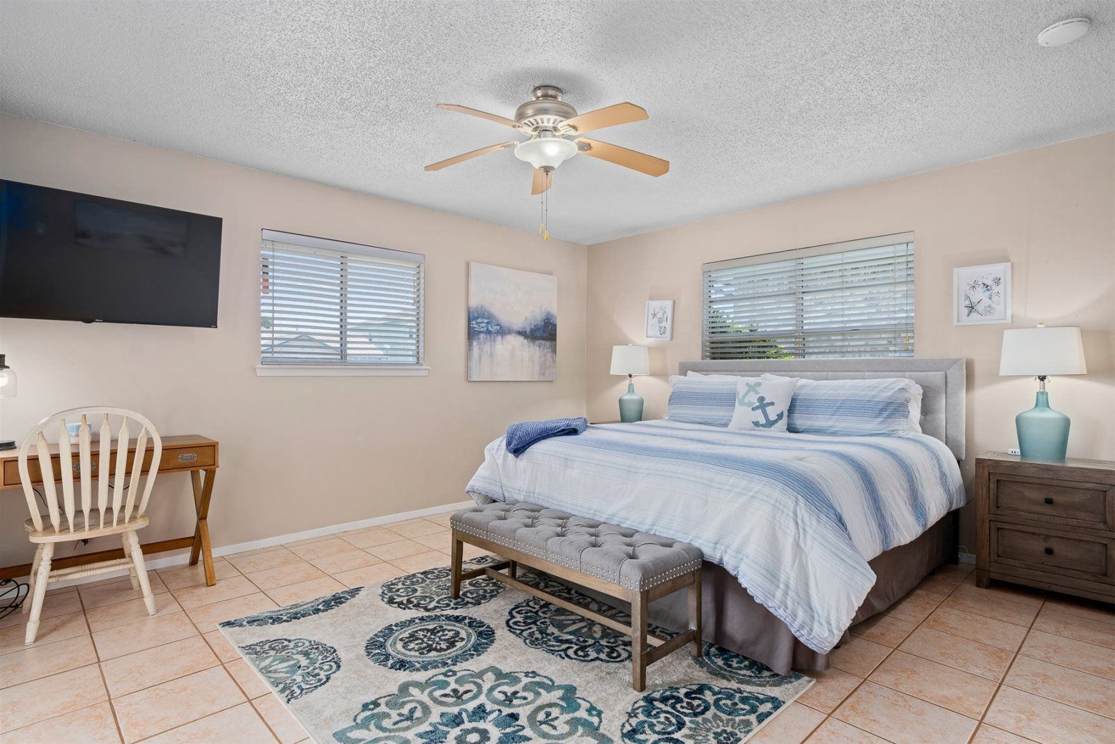 A bedroom with a bed, a desk, a chair, a ceiling fan, and a TV.