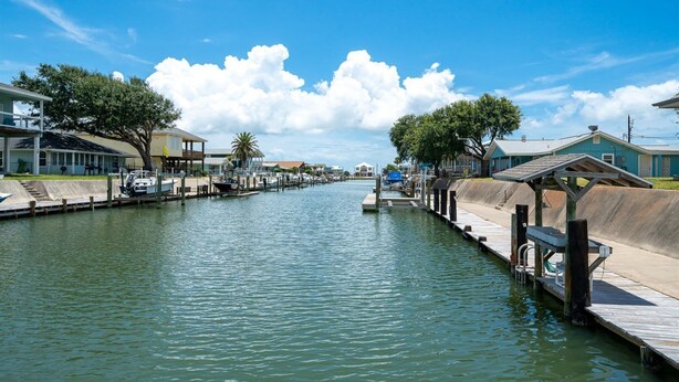 A marina with docked boats, a wooden walkway, and houses along the water. - Gone Coastal by Miss Kitty’s (Rockport)