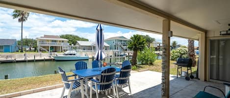 A covered patio with a table and chairs, overlooking a marina with boats and houses.