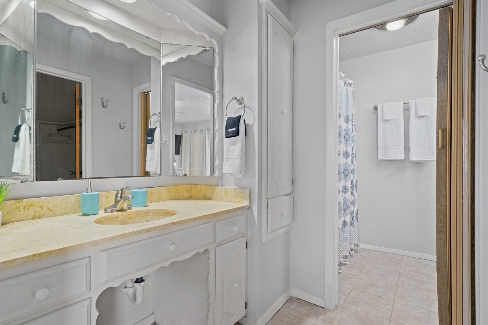 A bathroom with a large mirror, a sink with a faucet, a towel rack, and a shower curtain.