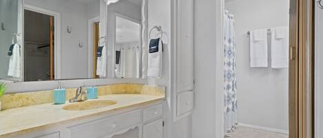 A bathroom with a large mirror, a sink with a faucet, a towel rack, and a shower curtain.